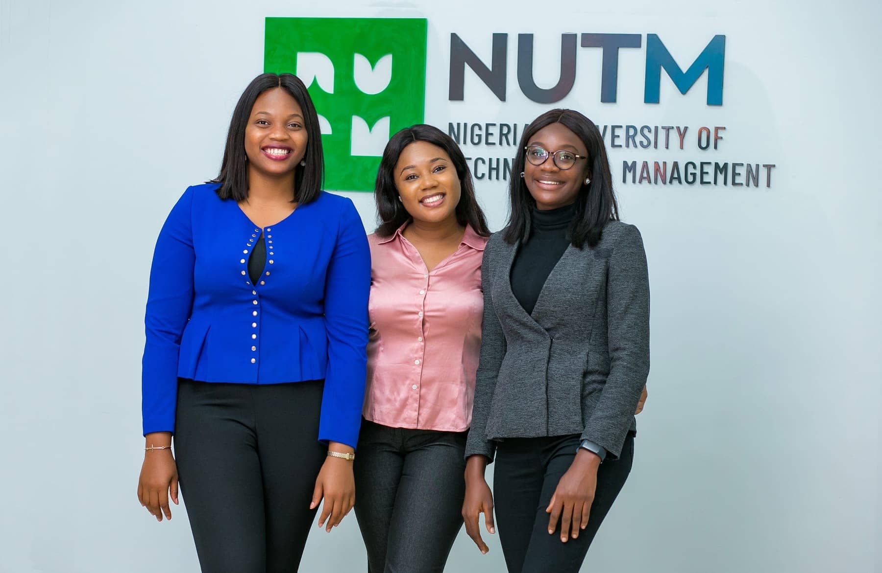 Three students in front of the NUTM sign