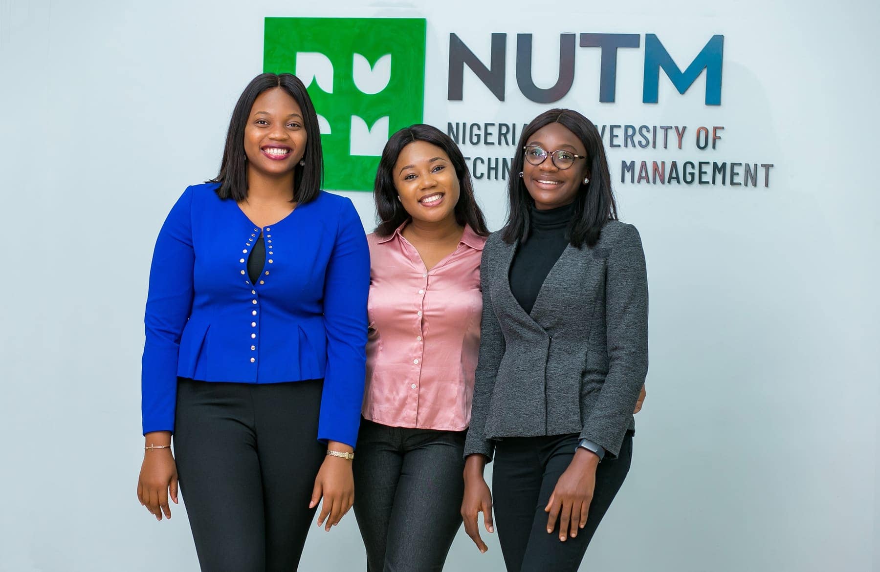 Three students in front of the NUTM sign